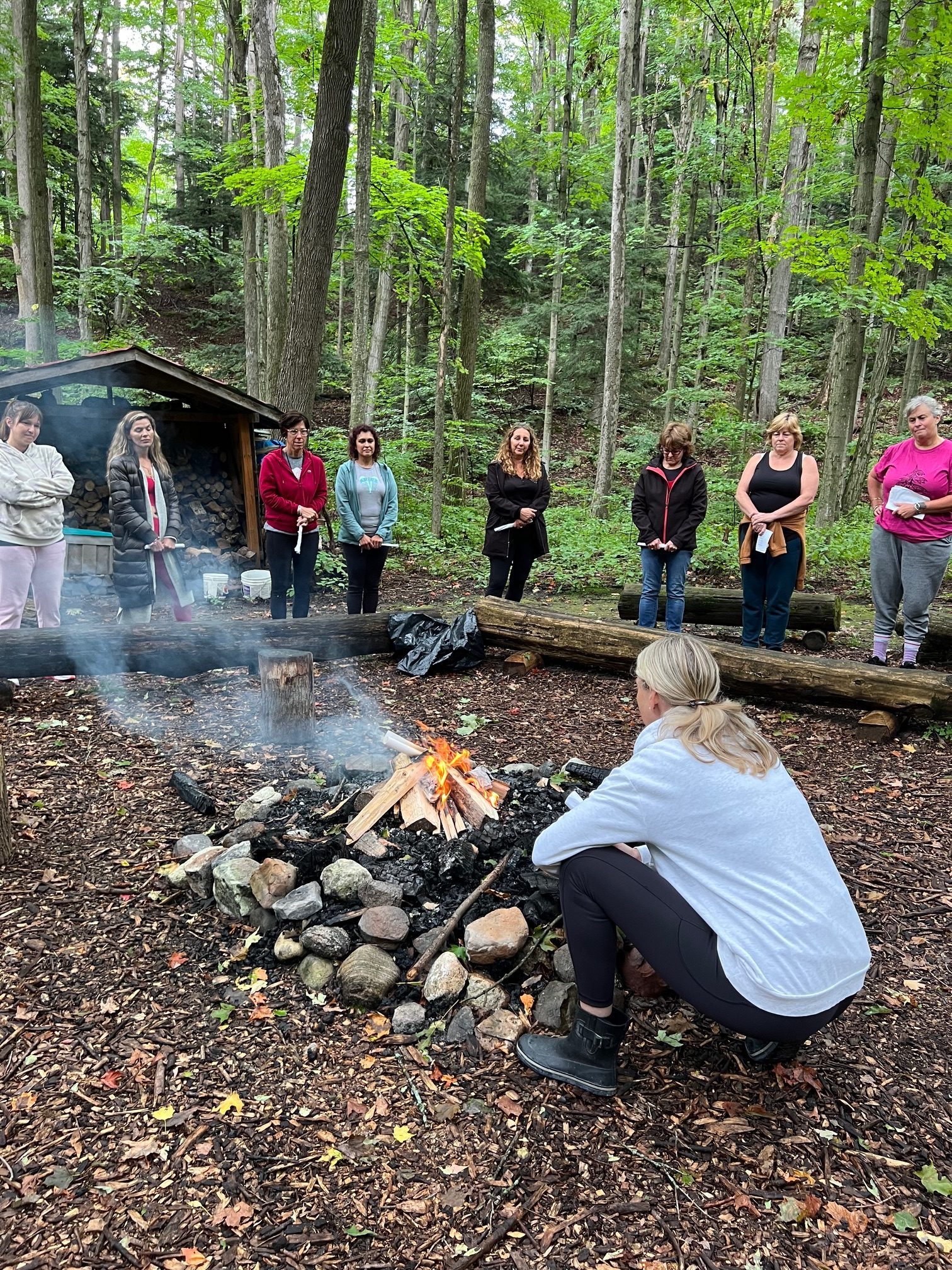 Women gathered around a ritual fire during the closing circle at The Goddess Retreat, with one woman crouched tending the flames in the foreground